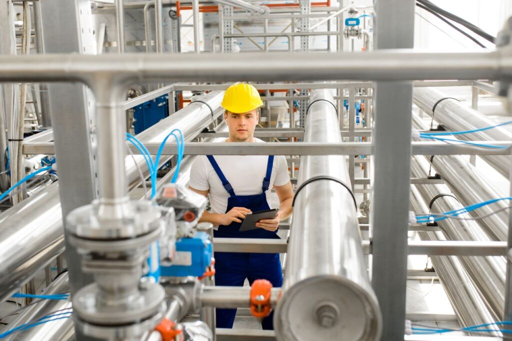 Techniker mit Schutzhelm ueberwacht Druckaufnehmer und Rohrsystem in moderner Produktionsumgebung